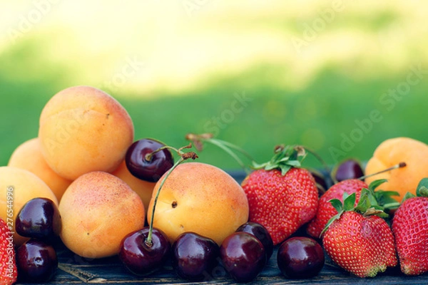 Fototapeta Juicy summer fruits and berries - apricots, cherries and strawberries lie in close-up against the background of a green lawn