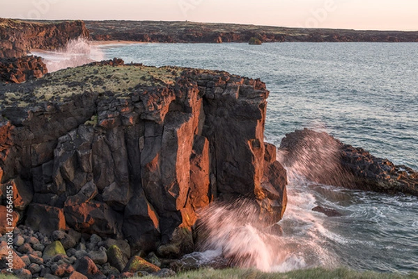 Obraz Low sun illuminated cliffs above a bay in Iceland. Close to midnight - long summer days, sun rays paint the cliffs red, with green vegetation above and Atlantic waves 