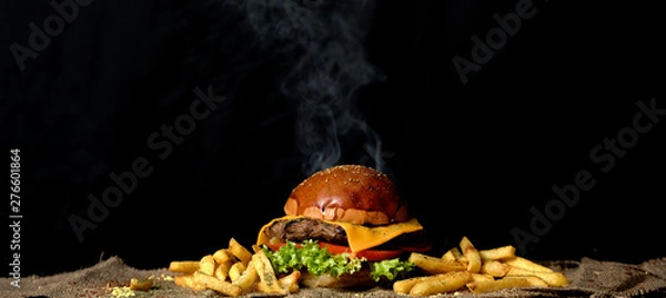 Fototapeta Giant delicious hot cheeseburger with tomato,lettuce,cheese and a big piece of meat served with french fries on a brown sack table mat on black background