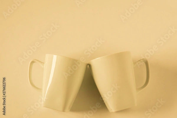 Fototapeta Yellow coffee mugs on yellow background clinking in cheers with empty copy space