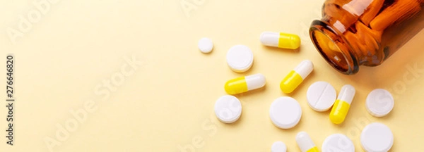 Fototapeta Multicolor tablets and pills capsules from glass bottle on yellow background Heap of assorted various medicine tablets and pills. Health care Close-up