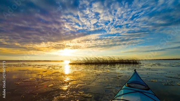 Fototapeta View from bow (prow) of blue kayak on lake with ice floes in winter or early spring at buatiful sunset. Winter kayaking