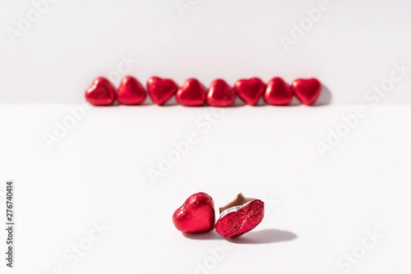 Fototapeta Heart shape chocolates wrapped in red foil on white background. Valentines day gift. Love and parting concept. Copy space.