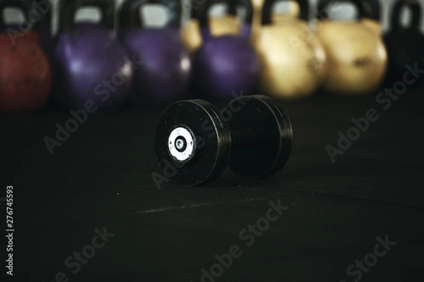 Fototapeta Gym equipment. The steel dumbbell stands  on the black rubber floor on the background of colorful weights.