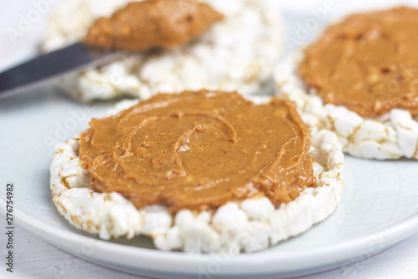 Fototapeta crunchy natural peanut butter sandwich with rice cake bread and knife with peanut butter on plate. Proper nutrition diet vegetarian breakfast