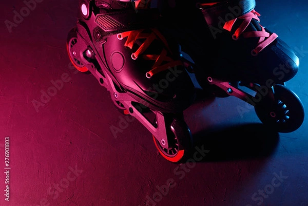 Fototapeta Close up view of roller skates inline skate or rollerblading on dark grunge background in neon blue magenta pink light