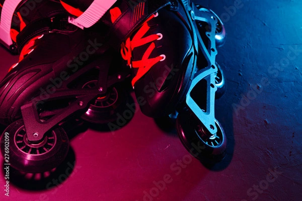 Fototapeta Close up view of roller skates inline skate or rollerblading on dark grunge background in neon blue magenta pink light