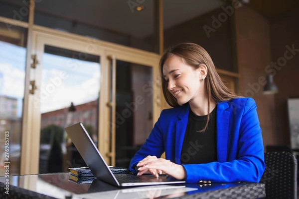 Obraz Beautiful business woman in a jacket sitting at a laptop and smiling