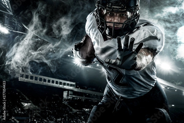 Fototapeta American football player. Sportsman with ball in helmet on stadium in action. Sport wallpaper. Closeup portrait.