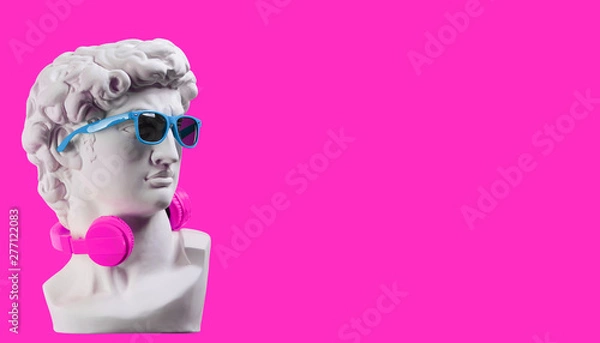 Fototapeta Statue. Earphone on a pink background. Gypsum statue of David's head. Creative. Plaster statue of David's head in blue sunglasses. Minimal concept art.