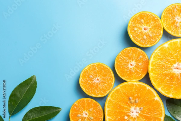 Fototapeta Sliced orange fruits with leaves on blue background, flat design