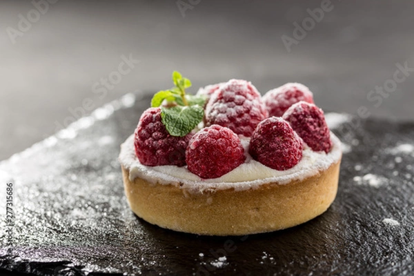 Obraz Raspberry tartlets with icing sugar close up on stone board on black background