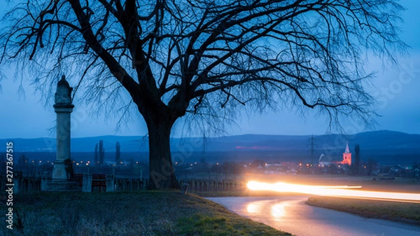 Fototapeta Lights of a car passing by an old way cross in Austria