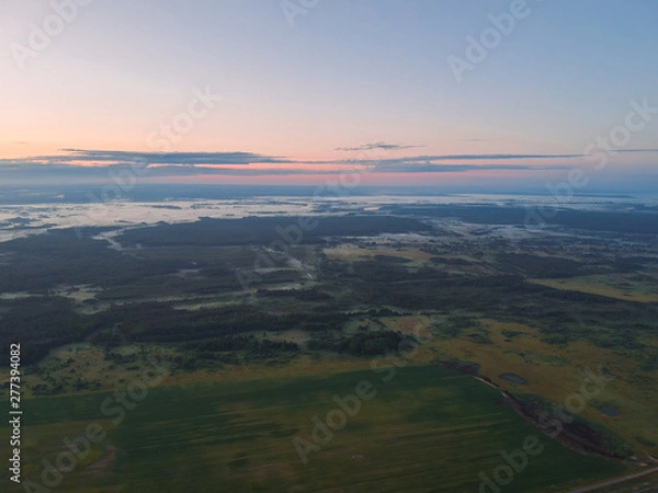 Fototapeta View from the height of the quadcopter on the landscape before dawn , fog dissipates in the fields near the forest.