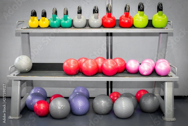Fototapeta Colorful kettlebells weights and fitness ball in a row on gym floor.