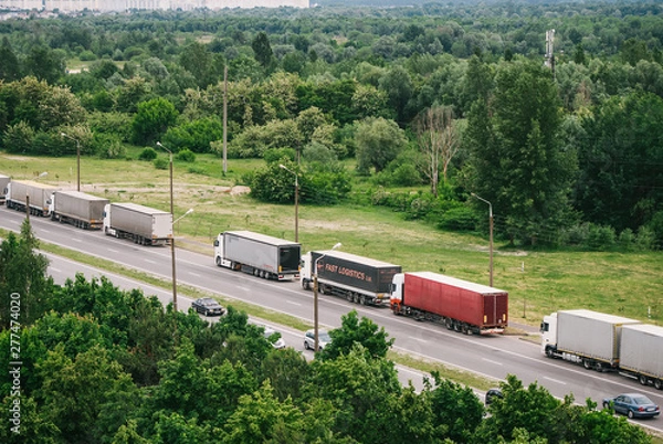 Obraz Queue of trucks passing the international border, red and different colors trucks in traffic jam on the road.