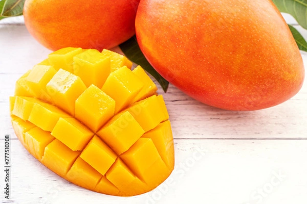 Fototapeta Beautiful chopped mango with green leaves on bright white color timber background. Above Top view, flat lay, copy space, close up. Tropical fruit concept.