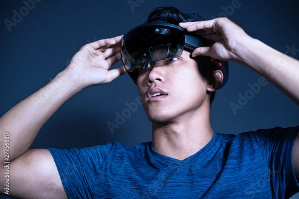 Fototapeta The Asian young man with glasses of virtual reality. Experience VR hololens headset in studio with advanced technology. Surprise face testing new device.