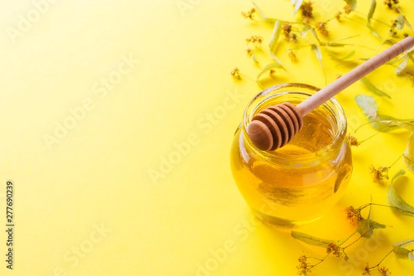 Fototapeta A jar of liquid honey from Linden flowers and a stick with honey on yellow background. Copy space