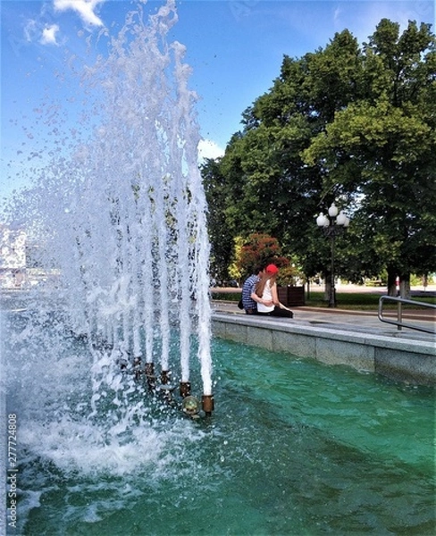 Obraz A loving couple, a guy and a girl, sit in a touching hug, and behind them are the braves of water from the fountain.