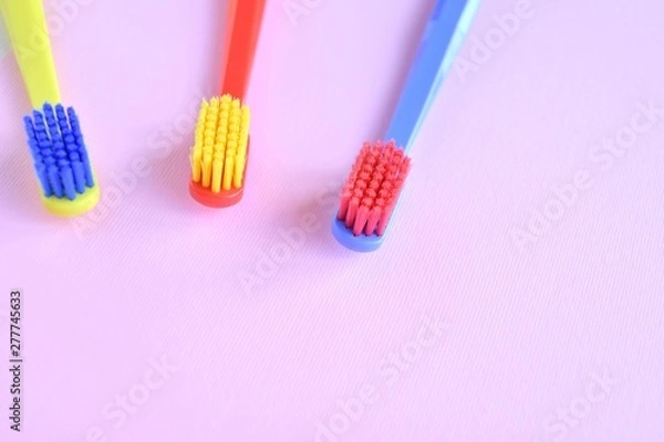 Fototapeta Three colorful plastic toothbrush with selective focus on blurred pink background. Multicolored toothbrushes for personal daily healthcare. Toothbrushes for daily oral hygiene and caries protection