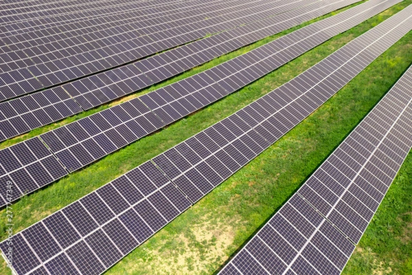 Fototapeta Solar panels in a field on the outskirts of a residential village in summer against the background of blue sky and power plants. Ecolongically clean energy production. Alternative energy sources
