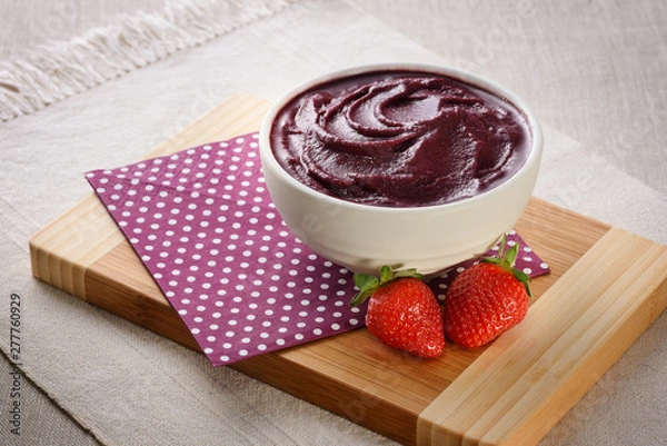 Fototapeta Açaí bowl with strawberries under napkin and wood board