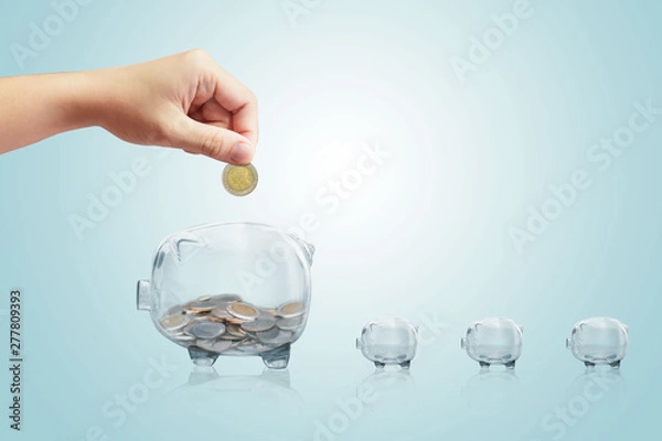 Obraz Hand puts a coin in the piggy bank on isolate background.Inserting a coin into a piggy bank