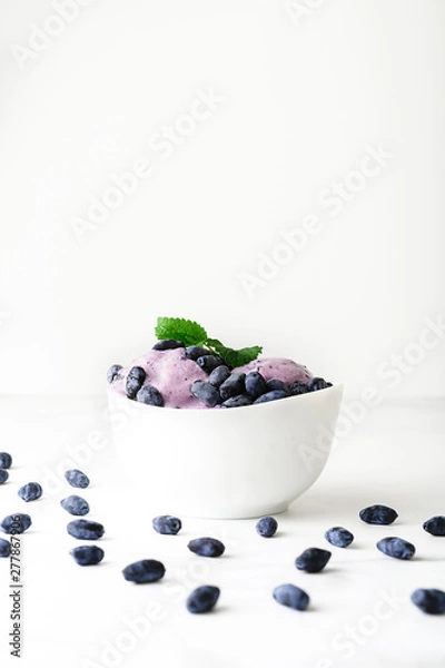 Fototapeta Ice-cream decorated with fresh berries of a honeysuckle and green leaves on white background. Close-up.