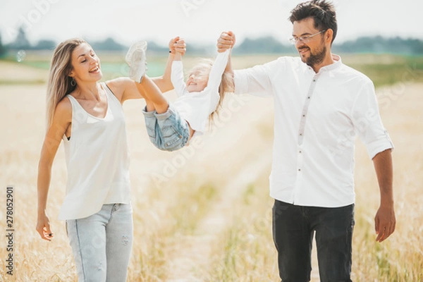 Obraz Father and mother throws up daughter in the sky in wheat field on sunny day.