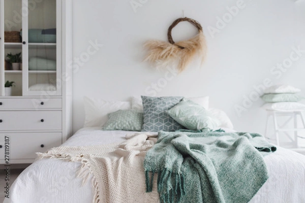 Fototapeta Modern scandinavian sunny bedroom with plants , floral pattern bedding and pilows. Space with white walls and eco decor. A bed with a mint plaid.