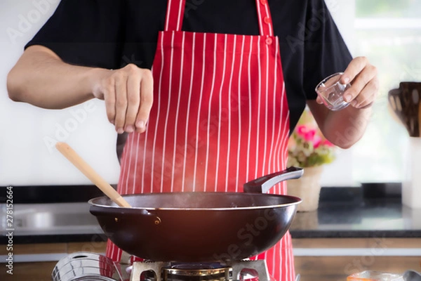 Fototapeta A man cooking food in the kitchen and adding some seasoning into a cooking pan