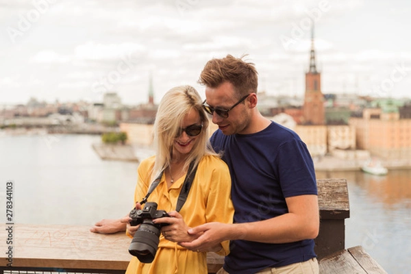 Fototapeta Portrait of the joyful young couple who is standing in the embrace against the background of the city and river and looking at the camera