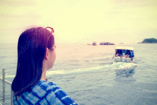 Fototapeta Back of Asian woman looking at the speed boat that sailed away from her, With a lonely, solitary, sad atmosphere during sunset in vintage style