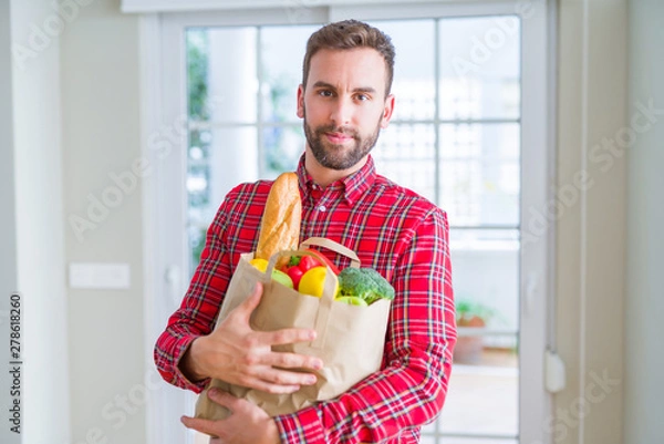 Fototapeta Handsome man holding groceries bag with a confident expression on smart face thinking serious