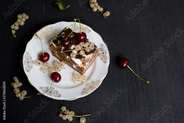 Fototapeta Top view of a slide of chocolate cake with a cherry on a white plate on a black background