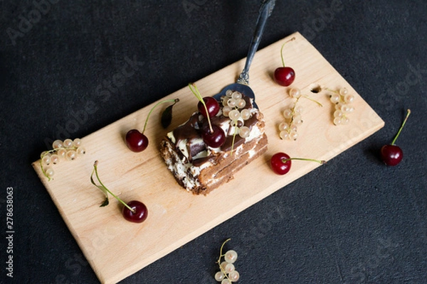 Fototapeta Top view of a slide of chocolate cake with a cherry on a black background