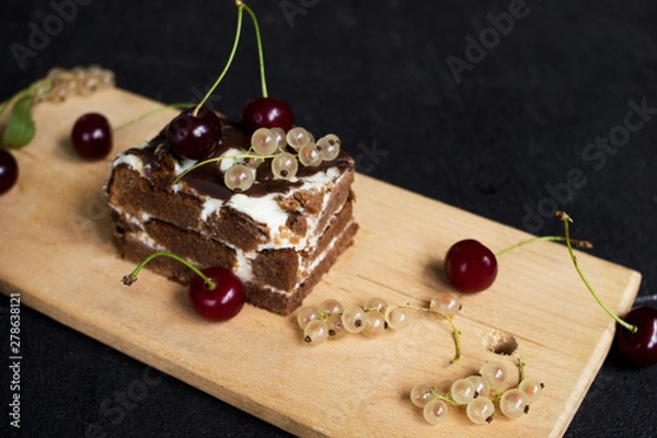Fototapeta A slide of chocolate cake with a cherry on a black background