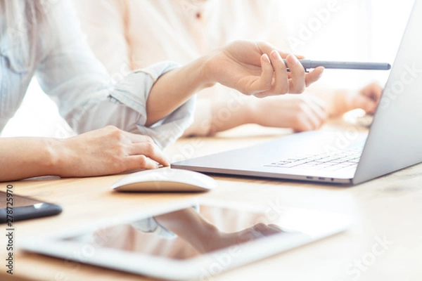 Obraz Girls dressed in casual discuss work issues, hands on a laptop