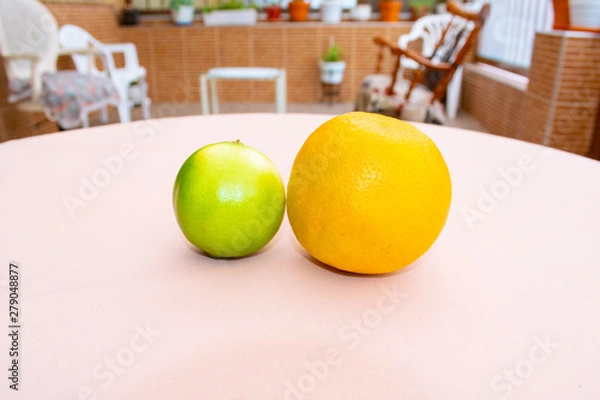 Fototapeta A green lemon and an orange close up with a colorful background