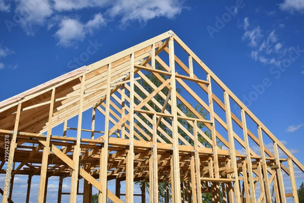 Obraz Wood frame residential building under construction.Building construction, wood framing structure at new property development site.new home currently under construction against blue sky.mortgage, loan.