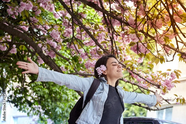 Fototapeta Young girl with arms wide open enjoying sunshine standing on the background of blooming sakura