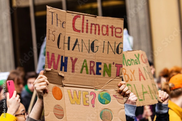 Fototapeta Homemade sign at environmental rally. A colorful cardboard placard is viewed close up, saying the climate is changing, why aren't we, in the hands of ecological activists as they protest in the city