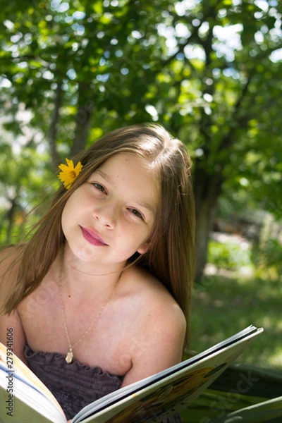 Fototapeta Beautiful girl reading a book and lying on a hammock in the garden