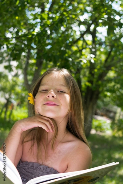 Fototapeta Beautiful girl reading a book and lying on a hammock in the garden