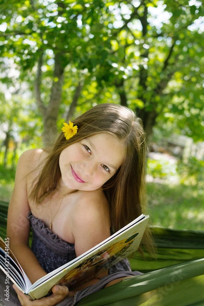 Fototapeta Beautiful girl reading a book and lying on a hammock in the garden