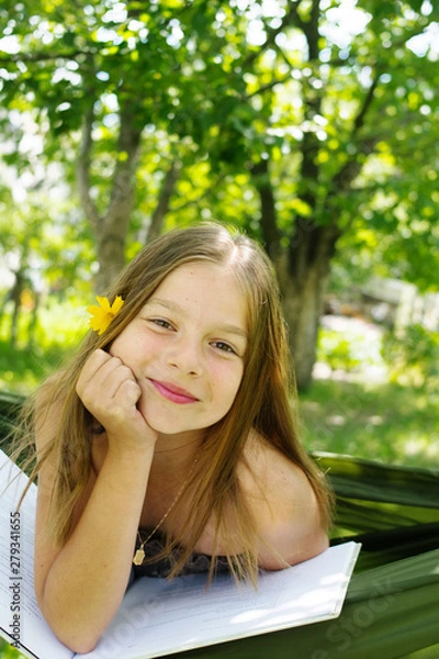 Fototapeta Beautiful girl reading a book and lying on a hammock in the garden