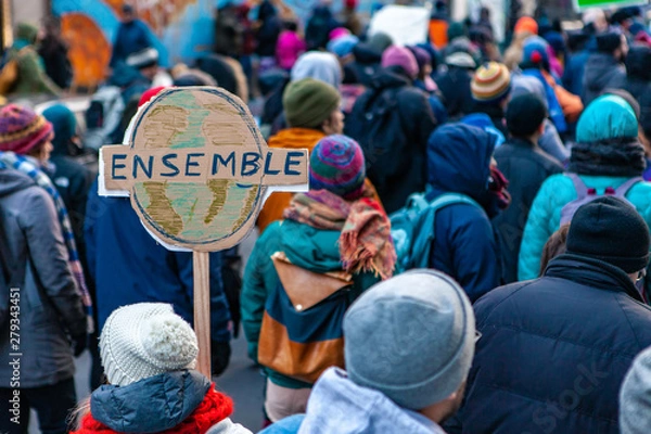 Fototapeta Environmental activists march in city. A French sign is seen close up, depicting planet earth and saying together, during a street demonstration by eco-activists, with copy space on the right
