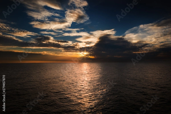 Obraz Ocean with sun setting through the clouds