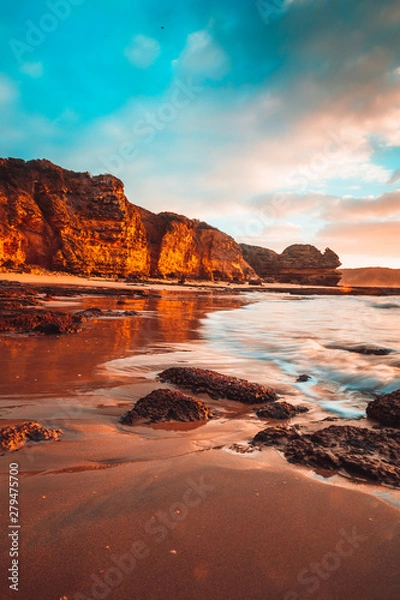 Fototapeta Waves washing over rocks at beach with cliffs in background
